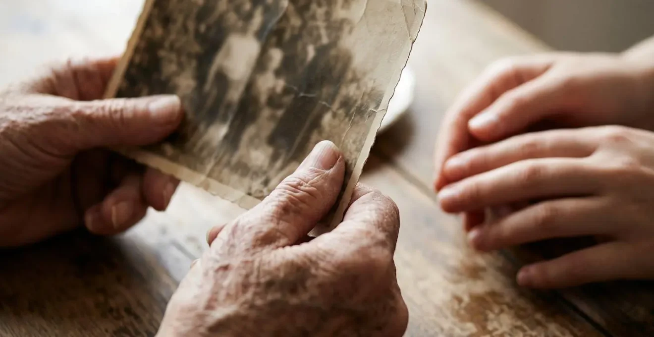 Elderly hands holding vintage family photograph while younger hands reach to gently touch the same photo, creating intergenerational connection